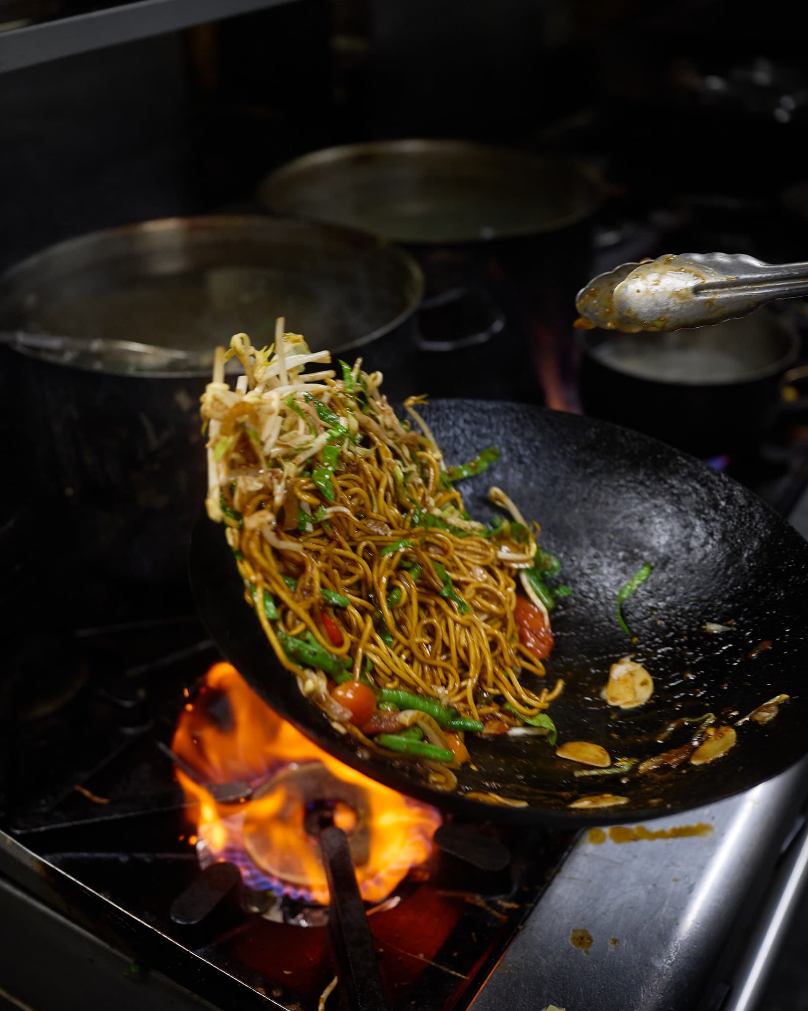 Noodles tossed in a wok over an open flame